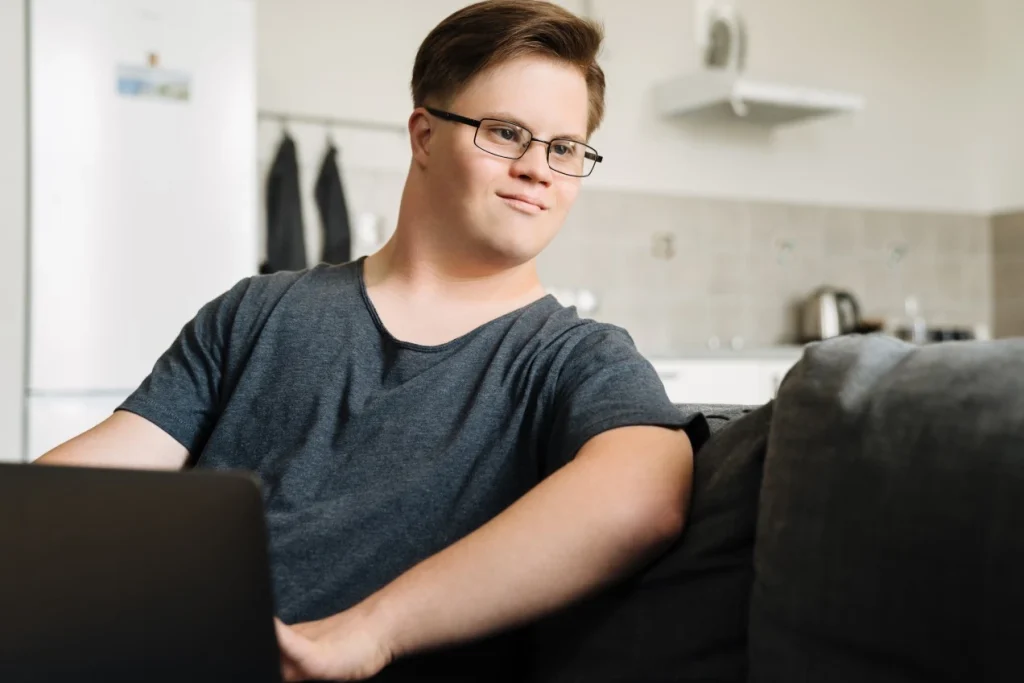 Disabled man with down syndrome sitting on couch using laptop