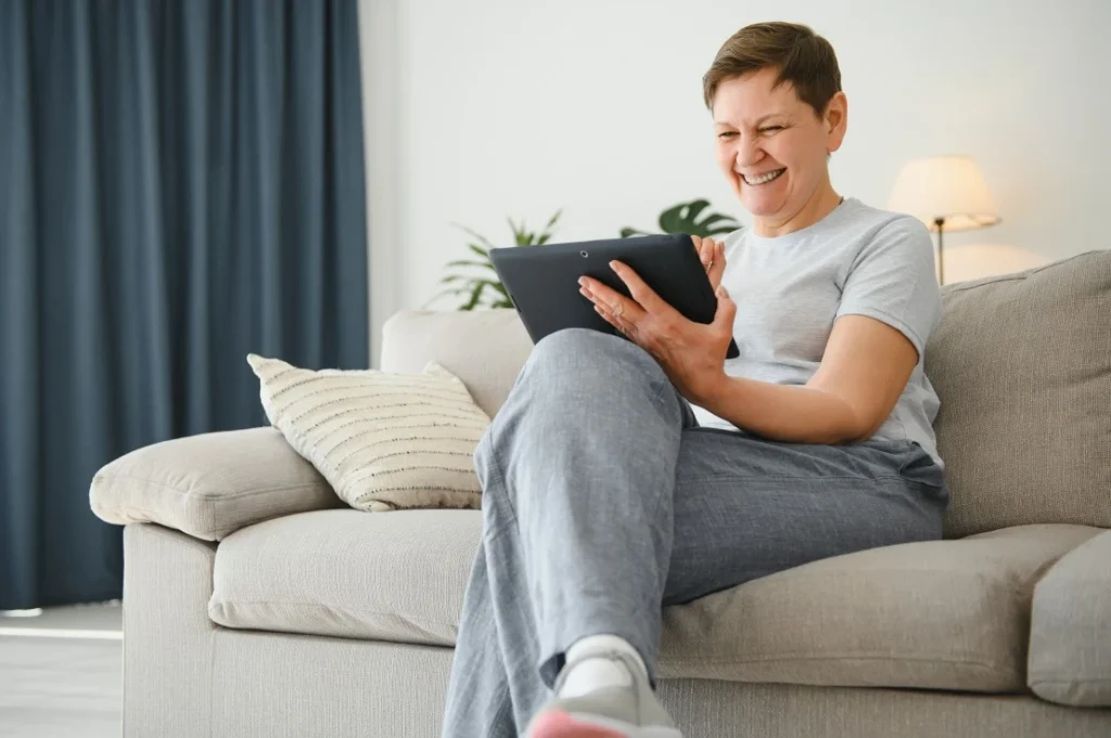 Happy woman sitting at home on couch looking at tablet