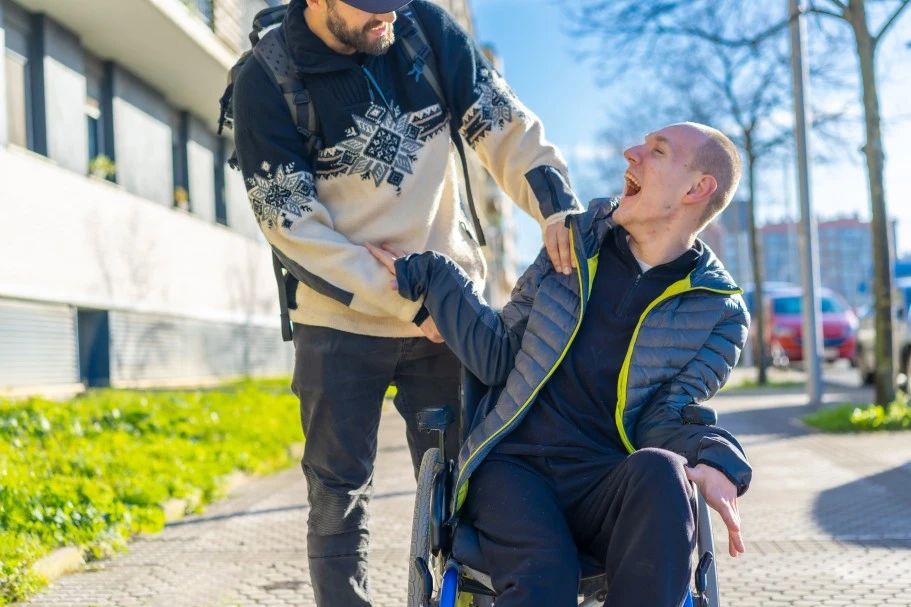 Disabled man in wheelchair laughing happily outside with support worker